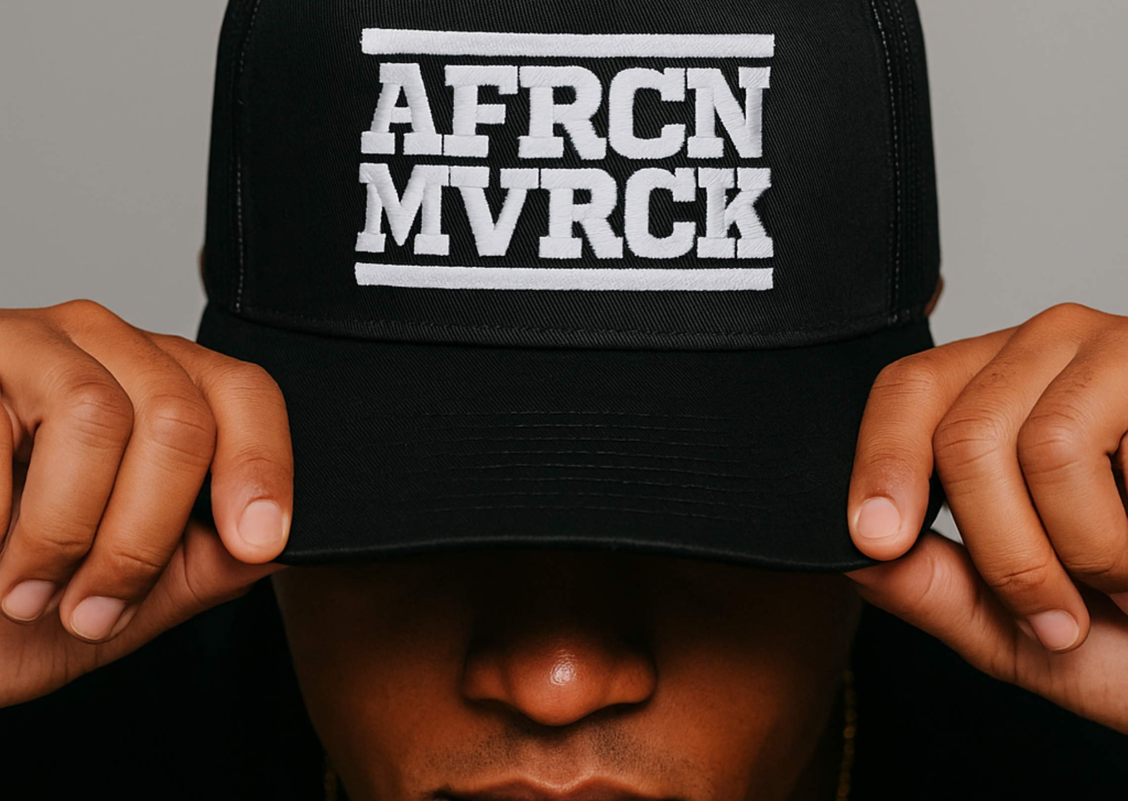 Black cap with 'AFRCN MVCK' text held by hands against a gray background. Streetwear for the African Diaspora
